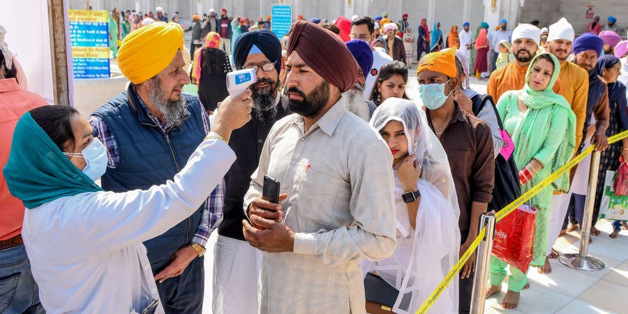 Perawat memeriksa suhu peziarah di pintu masuk Kuil Emas di Amritsar, India. foto: AFP via Getty Images