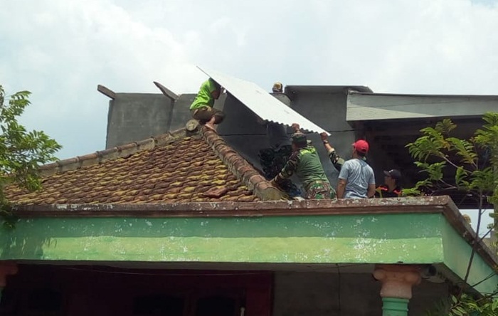 Warga dibantu petugas dari TNI yang sedang membetulkan atap asbes yang melorot.