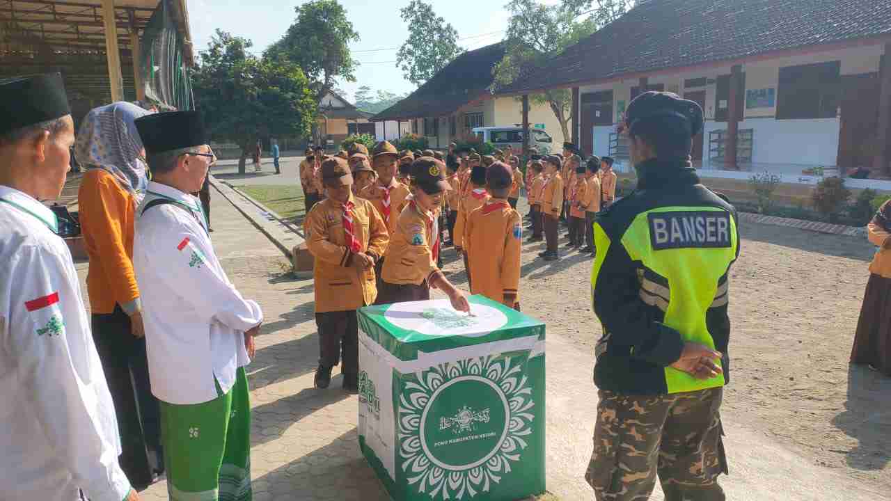 
Siswa MI Al Falah Desa Pagu, Kecamatan Wates, Kabupaten Kediri saat antri memasukkan koin ke kotak koin NU. (Ist).