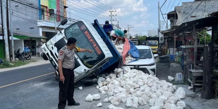 Truk muatan batu kapur yang terguling hingga menimpa sebuah mobil yang sedang terparkir