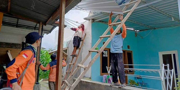 Petugas BPBD Kota Batu saat mengevakuasi atap TPS yang menimpa rumah warga.