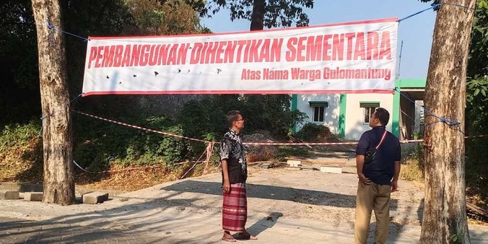 Ketua RW 2 Desa Gulomantung Muhammad Shofiudin dan Agus menunjukkan spanduk yang dipasang warga di depan bangunan Klinik Pratama MWC NU Kebomas. Foto: SYUHUD/ BANGSAONLINE