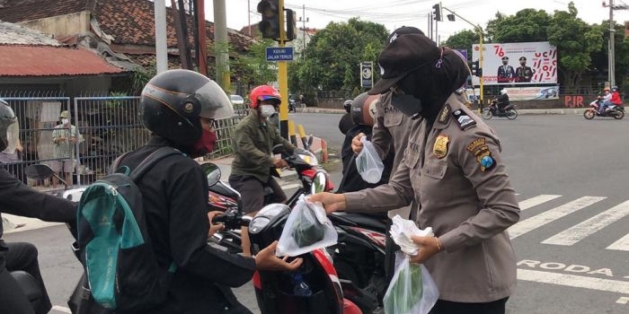 Petugas Polresta Banyuwangi saat membagikan nasi, air, dan masker kepada pengguna jalan