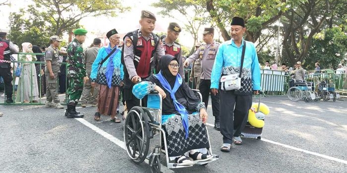 Salah satu calon jemaah haji dari Kabupaten Kediri saat dibantu petugas untuk menuju bus yang akan membawanya ke Surabaya. Foto: Ist