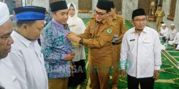 Bupati Pamekasan Baddrut Tamam saat memasangkan seragam kepada salah satu CJH. foto: ERRI/ BANGSAONLINE