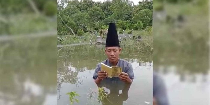 Hartono, warga Gading Watu, Kecamatan Menganti, Gresik, saat berdoa di makam yang terendam banjir. Foto: Ist
