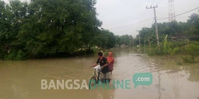 TETAP SETIA: Sepasang kekasih harus menuntun sepedanya untuk melewati banjir. foto: eki nurhadi/ BANGSAONLINE