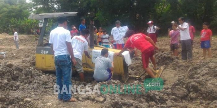 Sejumlah warga Dusun Kalangan, Desa Kalangsemanding, Kecamatan Perak menempel tulisan ke alat berat proyek berisi penolakan pembangunan perumahan daerahnya, Senin (2/1). foto: ROMZA/ BANGSAONLINE 