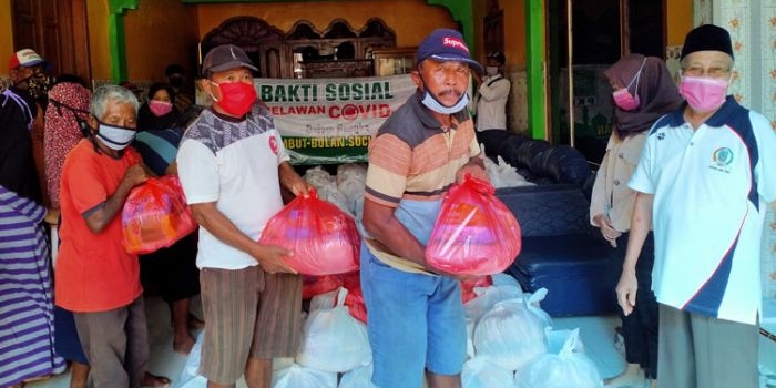 KH. Khusni (kanan) saat membagikan beras dan sembako pada para tukang becak dan warga kurang mampu di lingkungan rumahnya. foto: HERMAN/ BANGSAONLINE