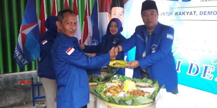 Ketua DPC PD Gresik Eddy Santoso saat menyerahkan tumpeng kepada Arif Rosyidi, kader baru. foto: SYUHUD/ BANGSAONLINE