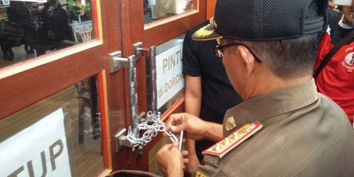 Kasi Penyelidikan dan Penyidikan Satpol PP, Mohammad Yusuf Wibiseno saat memasang gembok. foto: ERRI SUGIANTO/ BANGSAONLINE