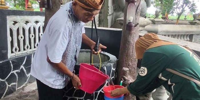 Juru Kunci Sendang Tirto Kamandanu, Mbah Gino, saat menuangkan air yang diambil dari sumber ke wadah milik salah seorang peziarah.