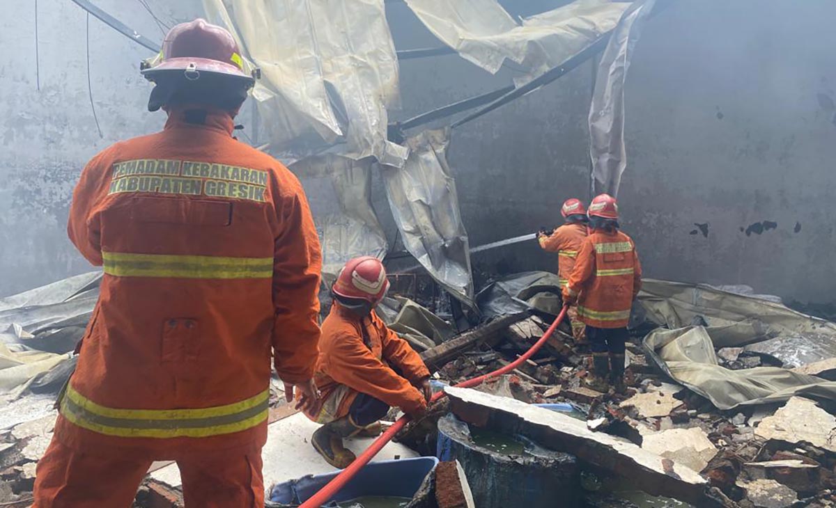 Petugas Damkar Gresik saat melakukan pembasahan gudang yang terbakar. Foto Ist.