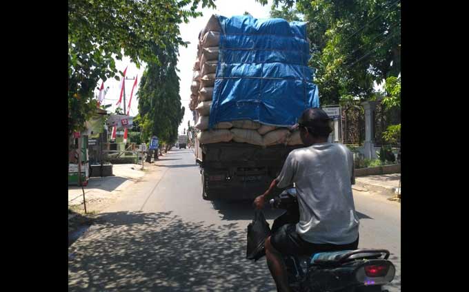 Pengendara motor tengah melintas di belakang truk bermuatan sekam. foto: HERI/ BANGSAONLINE