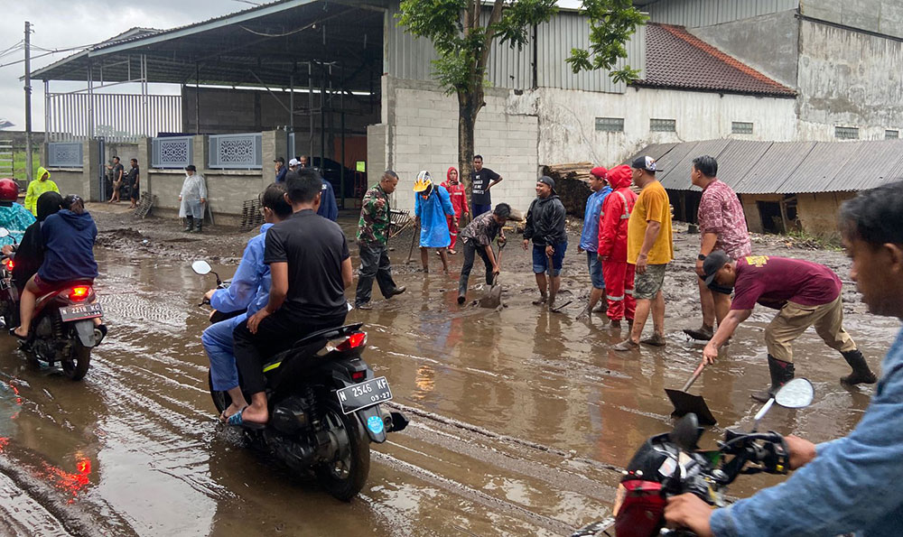 Petugas BPBD Kota Batu dibantu warga saat membersihkan lumpur yang sempat menutup jalan raya.