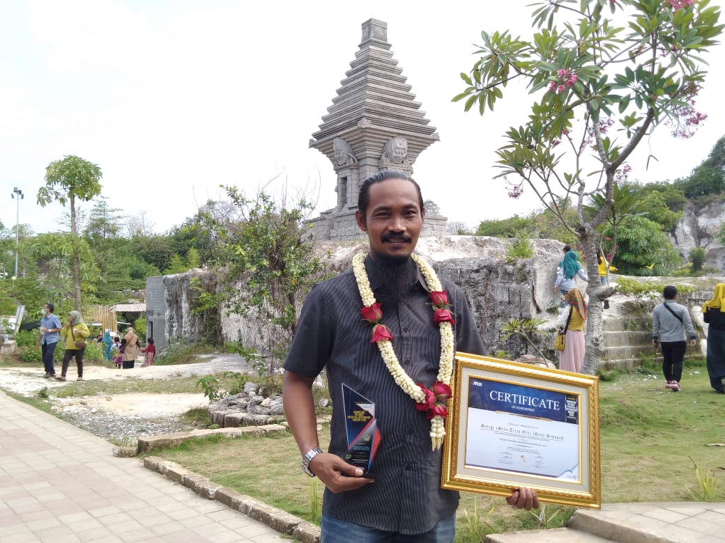 Kepala Desa (Kades) Sekapuk, Abdul Halim, bersama sertifikat penghargaan yang diraih selama ini berpose dengan latar belakang Wisata Setigi, bekas lahan tambang, di Desa Sekapuk, Kecamatan Ujungpangkah Kabupaten Gresik, Jawa Timur, Selasa (3/11/2020). foto: Syuhud Almanfaluty/ BANGSAONLINE