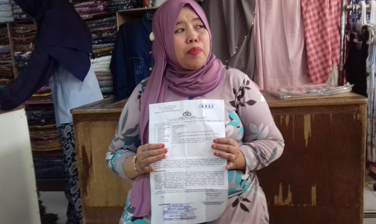 Korban menunjukkan bukti laporan kepolisian.