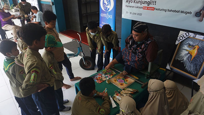 Pelukis difabel, Aam, saat menunjukkan kepiawaiannya melukis dengan kaki di kanvas. Foto: SYUHUD/BANGSAONLINE