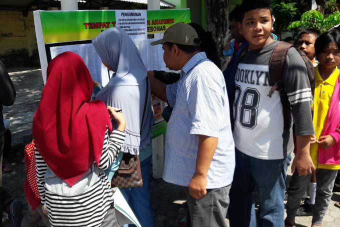 Para siswa dan orang tua saat melihat pengumuman hasil tes PPDB SMPN. foto: SYUHUD/ BANGSAONLINE