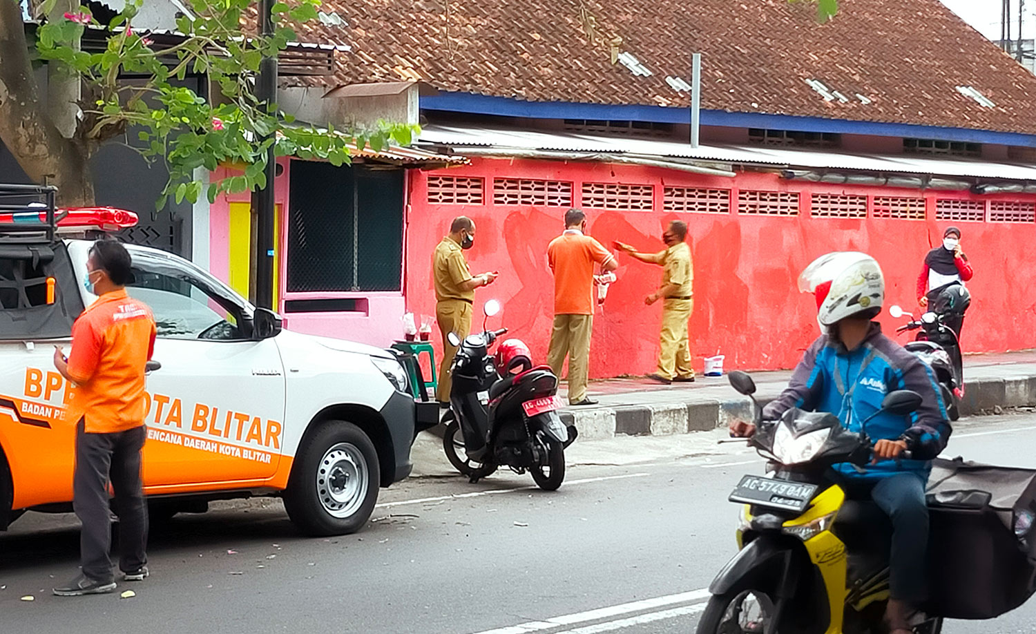 Tiga orang berseragam PNS tampak mengecat tembok yang sebelumnya berisi mural bernada kritik dengan cat warna merah.