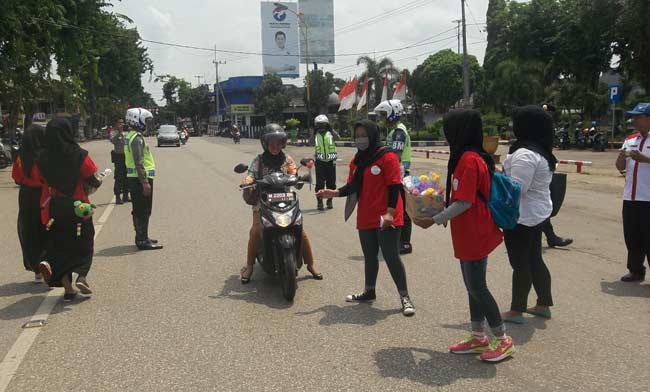 Siswa sedang membagikan rangkaian bunga pada pengendara jalan. foto: rahmatullah/ BANGSAONLINE