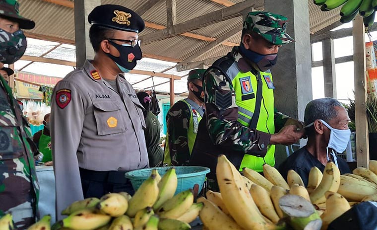 Kapolsek Gampengrejo, AKP Saiful Alam bersama Anggota Koramil Gampengrejo sedang memakaikan masker kepada pedagang pisang. foto: MUJI HARJITA/ BANGSAONLINE
