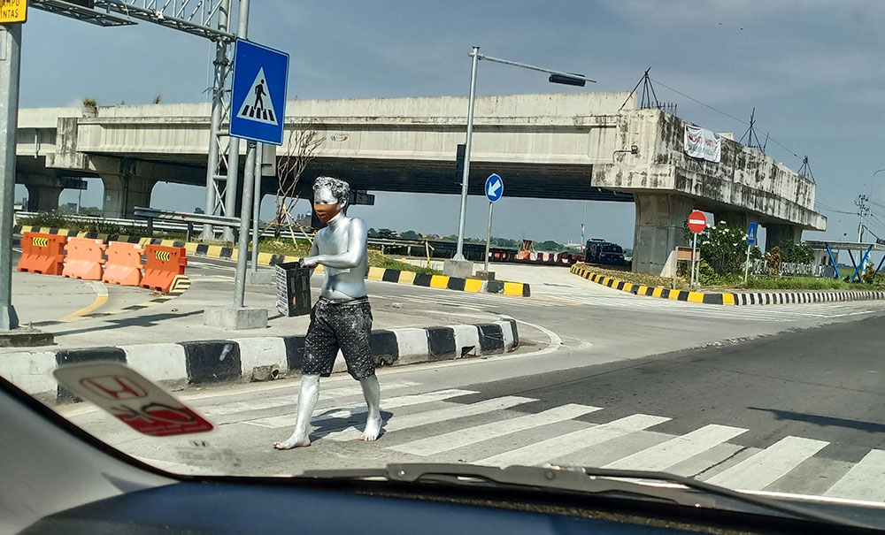 Salah satu manusia silver tampak sedang meminta-minta di Traffic Light Exit Tol Kebomas. foto: SYUHUD/ BANGSAONLINE
