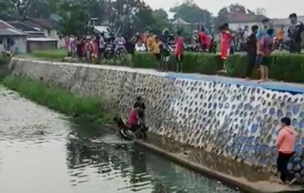 Pengendara motor yang nyungsep ke sungai saat ditolong oleh warga setempat.