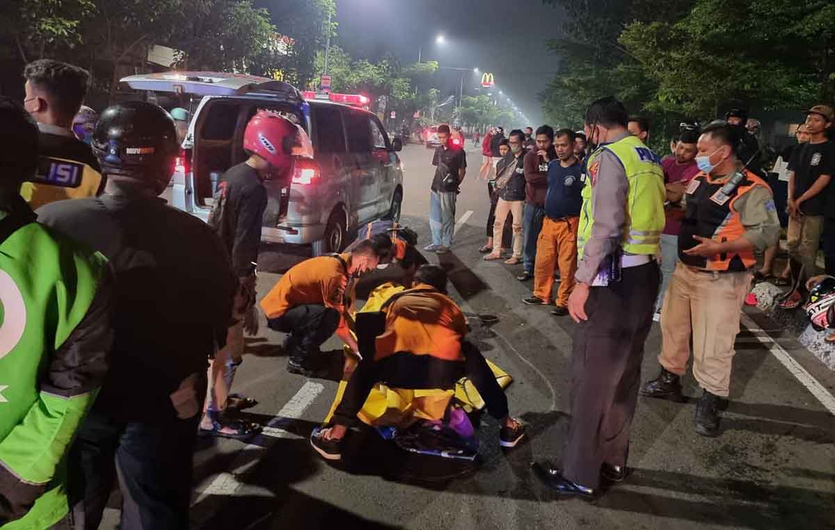 Petugas saat mengevakuasi pemotor yang tewas usai tabrak truk di Jalan Manyar Kertoarjo, Surabaya.