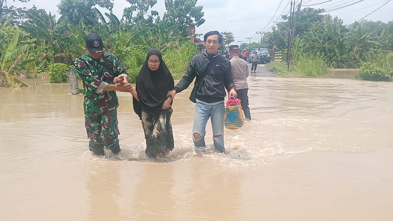 Personel Koramil 0817/09 Balongpanggang menuntun ibu-ibu melintas di jalan kebanjiran di Desa Wotansari, dampak luapan Kali Lamong. foto: ist.
