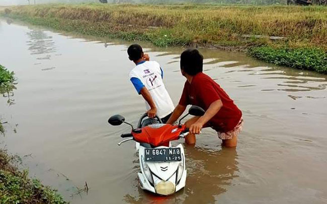 Warga saat mengevakuasi motor yang nyemplung ke sungai di Sidoarjo.
