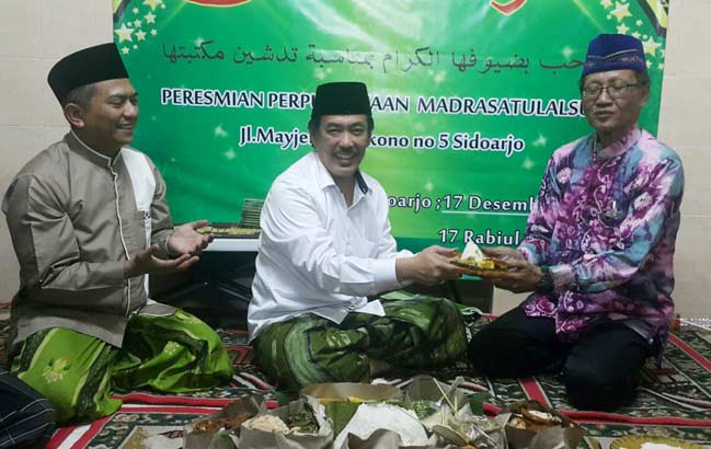 SIMBOLIS: Wabup Sidoarjo H Nur Ahmad Syaifuddin menyerahkan potongan tumpeng kepada H Mohammad Nasir Abdurrahman, kala peresmian Perpustakaan Madrasatulalsun, Sabtu (17/12). foto: mustain/ bangsaonline
