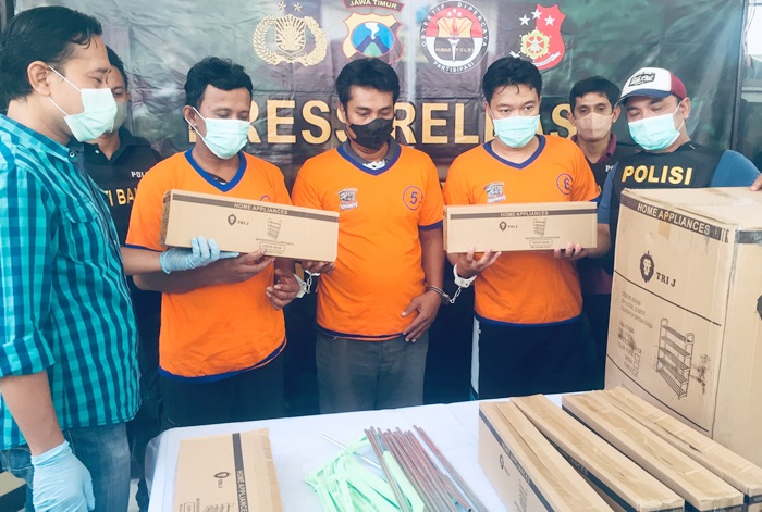 Ketiga tersangka diapit oleh petugas bersama barang bukti berupa rak sepatu yang masih dalam kemasan karton.