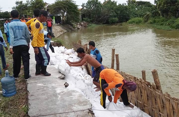 Warga dibantu petugas BPBD Lamongan saat menambal tanggul yang jebol.