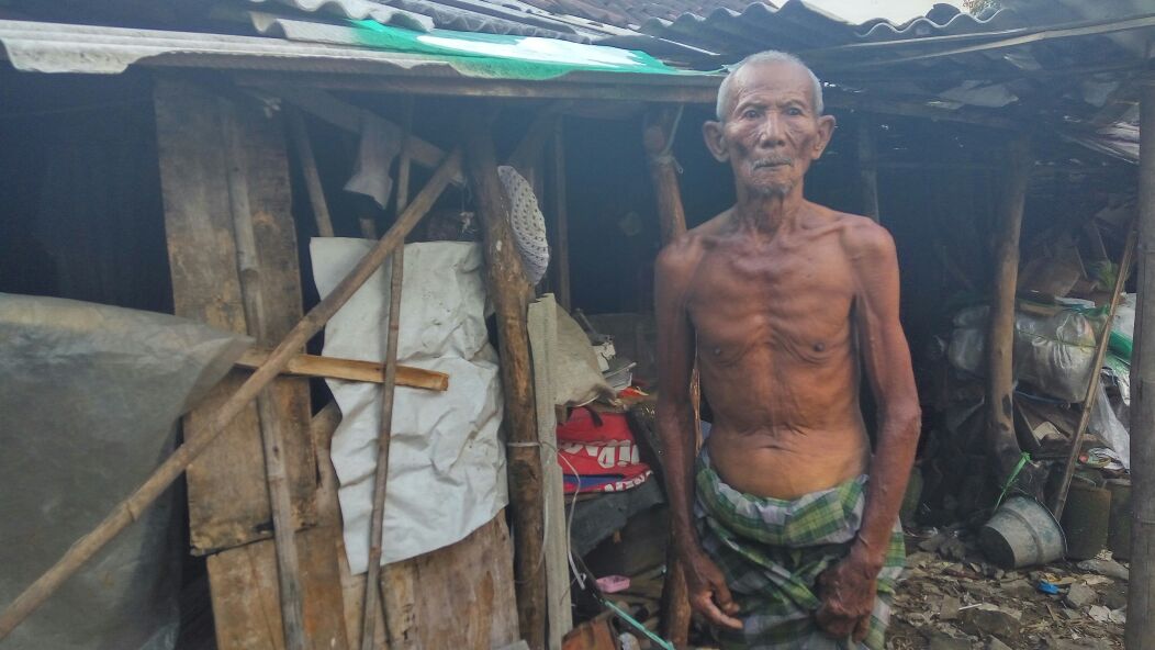 BUTUH PERHATIAN: Mbah Sular berdiri di depan rumahnya yang hanya disanggah menggunakan kayu dan berdinding triplek. foto: eky nurhadi/ BANGSAONLINE
