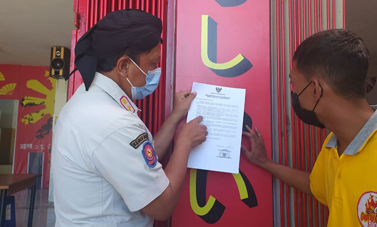 Kasatpol PP Trenggalek saat menempelkan surat seruan dari Bupati Trenggalek ke salah satu warung makan. (foto: HERMAN/ BANGSAONLINE)