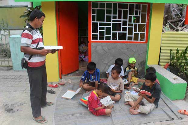 Anak-anak membaca buku di depan Poskamling RT 02 RW 01, Kelurahan Pandanwangi Blimbing Kota Malang dipandu langsung oleh Sutikno. foto: Istimewa