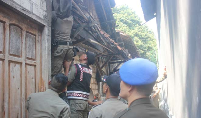 Petugas Satpol PP saat melakukan pemeriksaan di rumah yang diduga kuat masih memproduksi arak dengan menaiki genteng. foto: SUWANDI/ BANGSAONLINE
