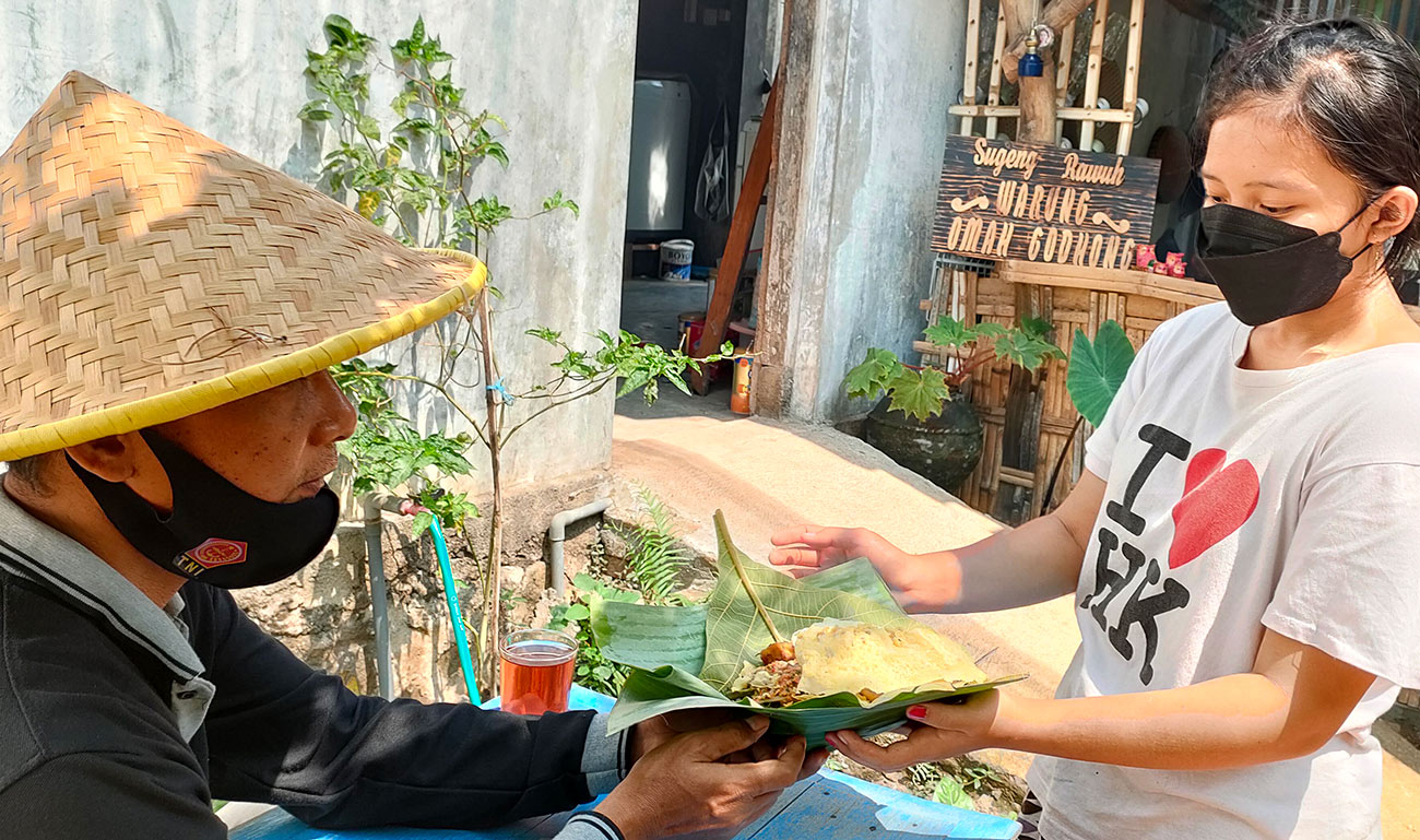 Anak Joni Lim yang turut membantu ayahnya, mengantarkan makanan kepada pelanggan yang memakai caping gunung. Foto: Muji Harjita/ bangsaonline.com