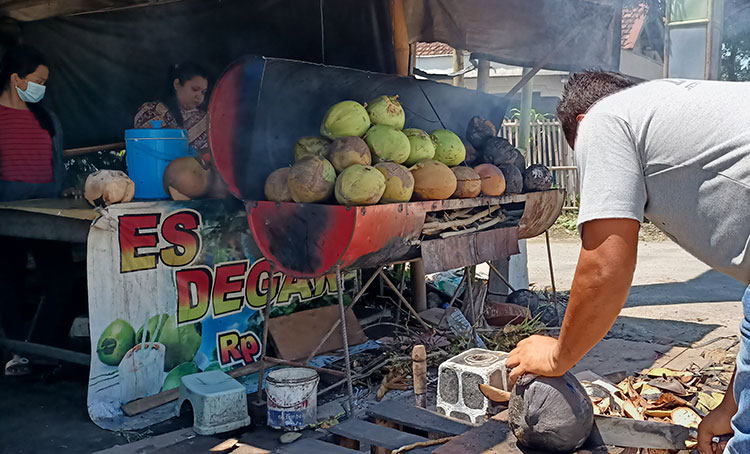Purwanto saat mengupas degan (kelapa muda) yang sudah dibakar. (foto: MUJI HARJITA/ BANGSAONLINE)