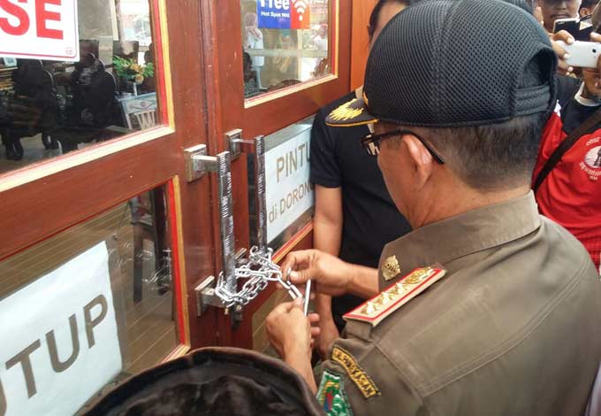 Kasi Penyelidikan dan Penyidikan Satpol PP, Mohammad Yusuf Wibiseno saat memasang gembok. foto: ERRI SUGIANTO/ BANGSAONLINE