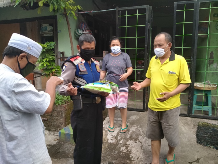 Salah satu aparat polisi sedang membagikan beras per orang 5 kg  dan uang Rp 50 ribu sedekah dari Kiai Asep Saifuddin Chalim, kepada warga Siwalankerto Utara Surabaya, Jumat (22/5/2020). foto: MMA/ BANGSAONLINE.COM
