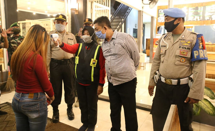 Petugas patroli gabungan saat melakukan pengecekan suhu tubuh pengunjung salah satu cafe.