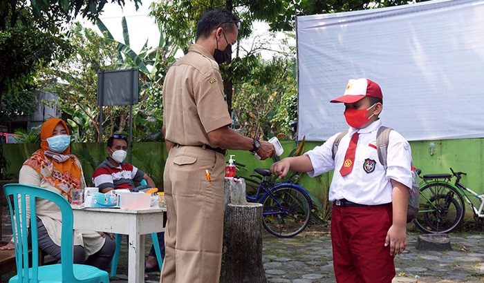 Salah seorang murid SD sedang dicek suhu tubuhnya dengan menggunakan thermogun sebelum masuk kelas oleh guru. foto: ist.