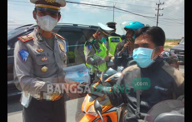 Kasat Lantas Polres Gresik AKP Anggi Saputro Ibrohim saat bagi-bagi masker di jalan Manyar. foto: SYUHUD/ BANGSAONLINE
