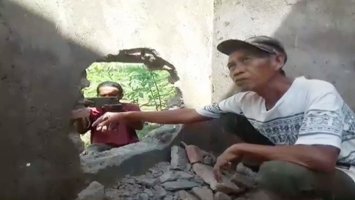 Seorang tukang sedang menunjukkan bagian tembok yang dibobol maling.